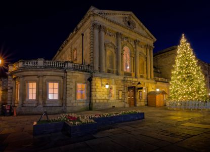 Un edificio storico di Bath illuminato accanto a un grande albero di Natale.