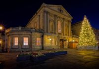 Un edificio storico di Bath illuminato accanto a un grande albero di Natale.