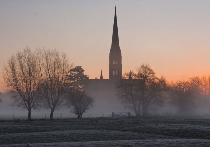 La guglia della cattedrale di Salisbury sopra la nebbia invernale all'alba